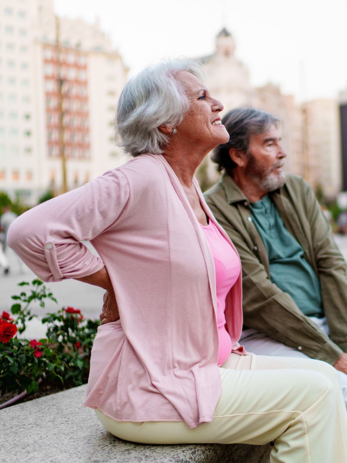 A woman on a bench with a hand on her lower back, her partner beside her