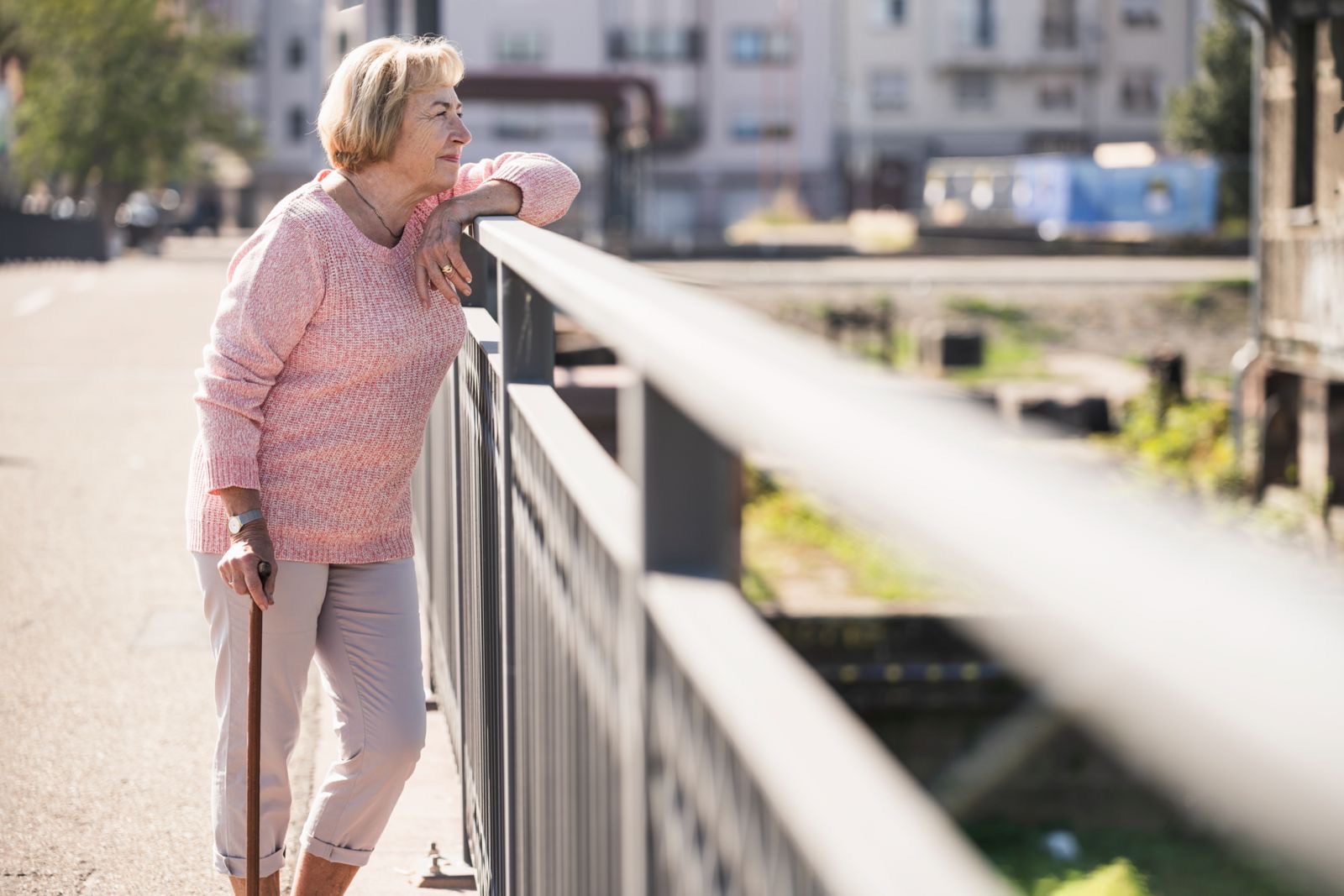 A woman with a cane resting her arm on a bridge railing